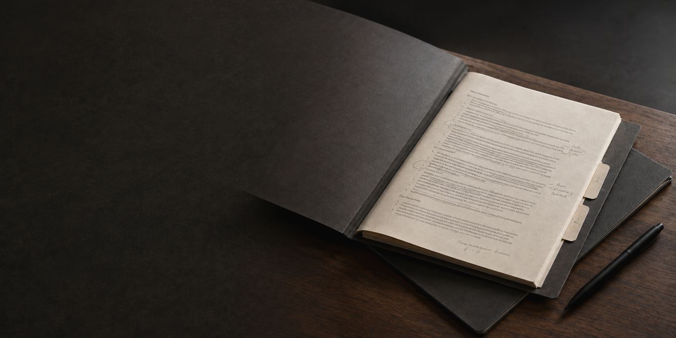 An open file on a dark desk, a document inside it with passages circled and notes written down the margin, two numbered tabs marking sections, a second folder beneath and a pen alongside